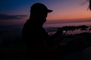 man in black shirt and black hat sitting on ground during sunset