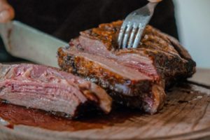 person slicing a meat on brown wooden board