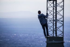 man climbing on tower near buildings at daytime